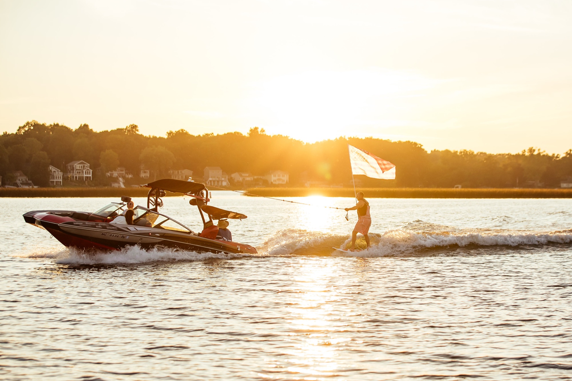 A boat pulling a wake surfer at golden hour on a calm Minnesota lake